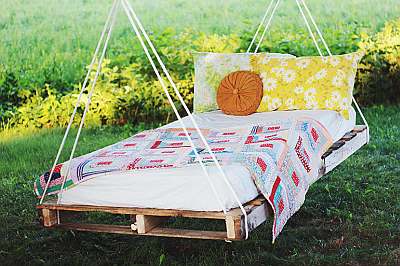 Pallets aan touwen onder een boom als schommelbed.